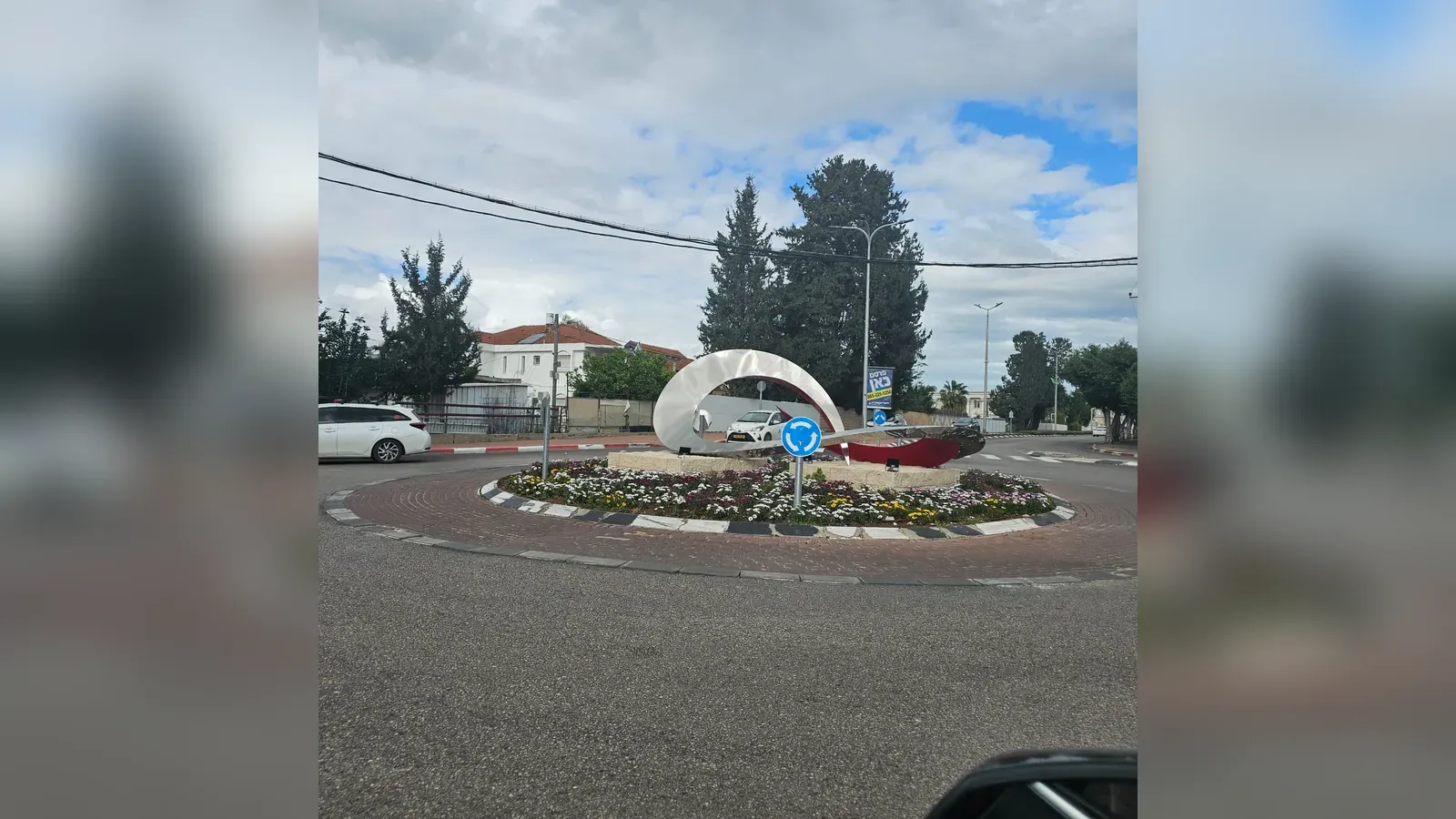 כיכר בעפולה ובמרכזה פסל קשת לבן, מוקף ערוגת פרחים עונתיים